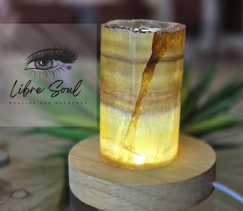 May include: A yellow and brown calcite crystal lamp on a wooden base. The lamp is lit and emits a warm glow.