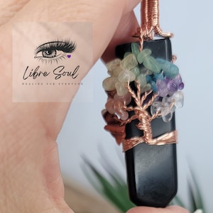 Op de afbeelding: Een zwarte obsidianen levensboom hanger met koperen draadwikkeling en een verscheidenheid aan gekleurde edelstenen, waaronder amethist, rozenkwarts en groene aventurijn.