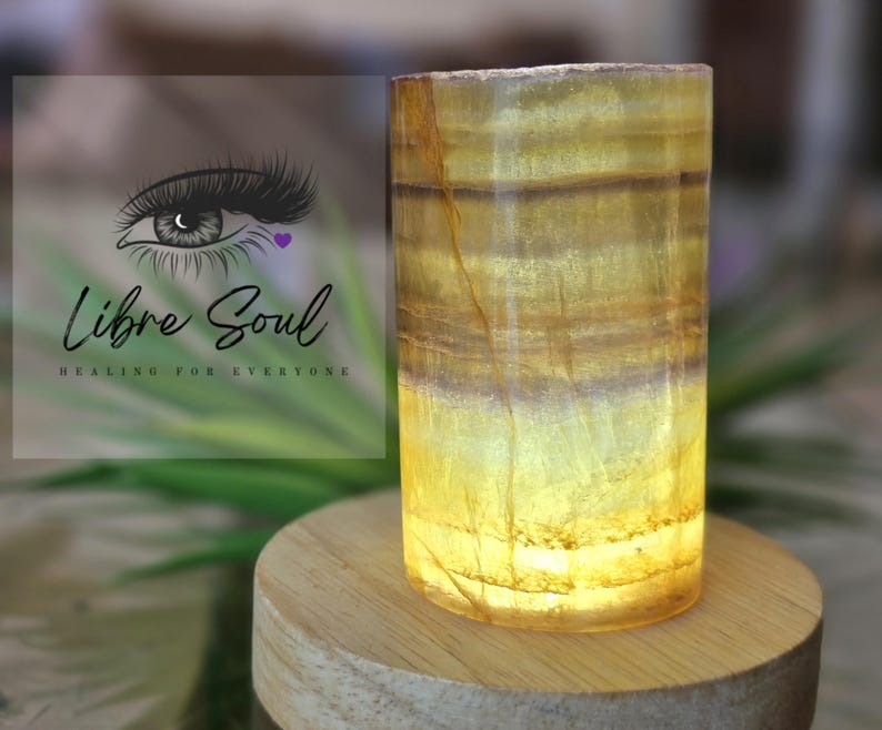 May include: A yellow and brown striped crystal lamp with a wooden base. The lamp is lit and glowing.