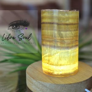 May include: A yellow and brown striped crystal lamp on a wooden base. The lamp is lit and glowing.