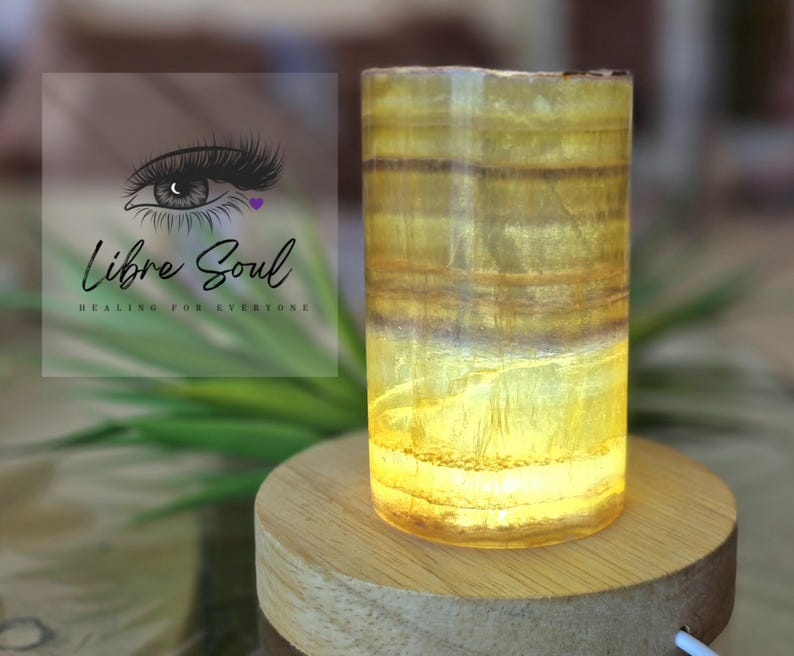 May include: A yellow and brown striped crystal lamp on a wooden base. The lamp is lit and glowing.