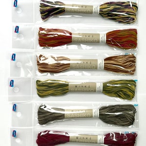 Könnte beinhalten: Zehn Spulen Sashiko-Garn in verschiedenen Farben, darunter Grün, Braun, Rot und Blau. Jede Spule ist mit "Sashiko" und "刺し子糸" beschriftet.