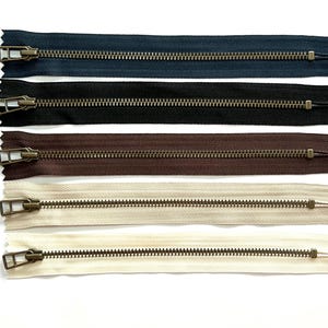May include: Five different zipper tapes with antique brass sliders. The tapes are navy blue, black, brown, cream, and white.