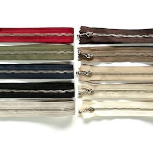 Könnte beinhalten: Eine Auswahl an Reißverschlüssen in verschiedenen Farben, darunter Rot, Olivgrün, Marineblau, Schwarz und Creme. Die Reißverschlüsse haben silberfarbene Metallzähne und -schieber. Geeignet für Näh- und Bastelprojekte.