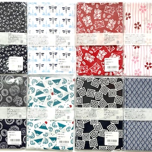 May include: Eight rectangular fabric cloths packaged in clear plastic, each featuring distinct Japanese-inspired patterns including dragonflies, maneki-neko cats, cherry blossoms, fireworks, mountains, geometric squares, and wave motifs.