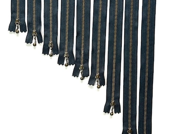 May include: A set of ten black zipper closures with brass pulls. The zippers are arranged in a diagonal line, with the shortest zipper at the top and the longest zipper at the bottom.