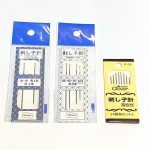 Pode incluir: Três pacotes de agulhas de costura sortidas, etiquetados "刺し子針" (Sashiko Needle) em japonês. Os pacotes são azuis, brancos e amarelos com texto preto. As agulhas são prateadas e douradas.
