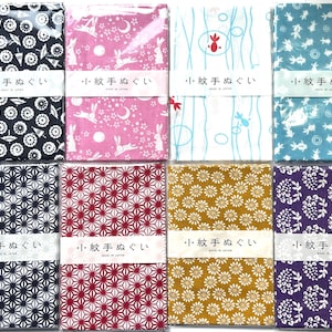 May include: Eight rectangular fabric cloths with diverse patterns including black umbrellas, pink rabbits, blue fish, and floral motifs. Each cloth is wrapped in a white paper band featuring the Japanese text 小紋手ぬぐい and MADE IN JAPAN.