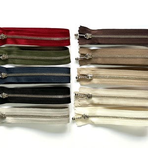 May include: Assortment of ten zipper closures in various colours, including red, brown, green, blue, black, and white. The zippers are all metal and have a silver finish.