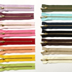以下が含まれることがあります： ピンク、赤、黄色、緑、青、茶色など、さまざまな色のジッパー14個の詰め合わせ。ジッパーには金色の金属製のスライダーが付いており、2列に並べてあります。