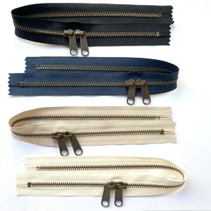 Może przedstawiać: Cztery zamki błyskawiczne w różnych kolorach: czarny, granatowy i dwa odcienie beżowego. Zamki błyskawiczne mają metalowe suwaki i są dwustronne.