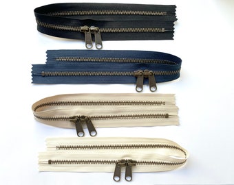 May include: Four zipper closures in different colours: black, navy blue, and two shades of beige. The zippers have brass pulls and are double-ended.