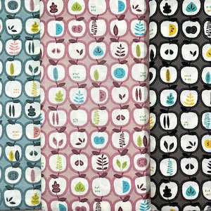 May include: Three fabric swatches featuring a repeating pattern of stylised apples, leaves, and geometric shapes. The swatches are in shades of blue, pink, and grey.