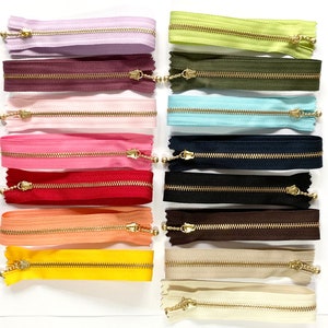 Puede incluir: Surtido de 14 cintas de cremallera con tiradores de metal dorado. Las cintas de cremallera son de varios colores, incluyendo rosa, rojo, azul, verde y beige.