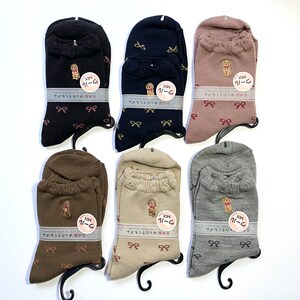 May include: Six pairs of socks with a bow pattern and a small dog embroidered on the front. The socks are in various colors including black, brown, beige, gray, and pink. Each pair has a tag with the text "MIX 11-24" and "ゆったりくもゴム 日本製" in Japanese.