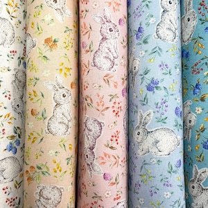 May include: Four fabric swatches featuring a repeating pattern of bunnies and flowers. The swatches are in shades of white, beige, pink, and blue.