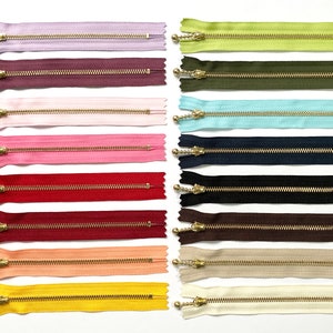 Puede incluir: Surtido de 18 tiradores de cremallera dorados con cintas de cremallera de diferentes colores. Las cintas de cremallera son de los siguientes colores: lavanda, burdeos, rosa, rosa claro, rojo, granate, melocotón, amarillo, beige y blanco.