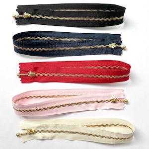 Puede incluir: Cinco cintas de cremallera de diferentes colores con cremalleras de metal dorado. Los colores son negro, azul marino, rojo, rosa y crema.