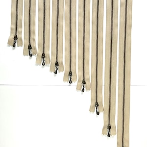 Puede incluir: Surtido de diez cierres de cremallera beige con tiradores de latón antiguo. Las cremalleras varían en tamaño de 12,7 cm a 45,7 cm.