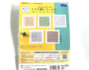 May include: A Sashiko sampler kit with the text "WEAVING Sashiko Sampler" and "くぐり刺しコースター". The kit includes instructions and materials to create embroidered coasters. The finished size is approximately 4 inches x 4 inches. The package features examples of finished designs.
