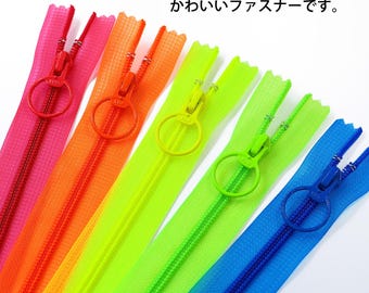 May include: A set of five neon-colored zippers in pink, orange, yellow, light green, and blue. Each zipper features a matching circular pull tab and a translucent, clear-toned plastic tape. The Japanese text reads: ネオンカラー × クリア感がかわいいファスナーです。
