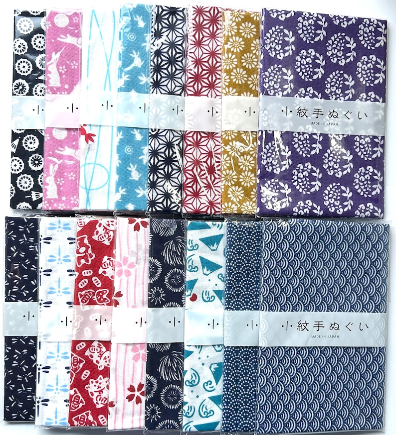 May include: A collection of sixteen rectangular cotton cloths, known as tenugui, arranged in two rows. Each cloth features distinct patterns including rabbits, flowers, geometric shapes, and waves, all wrapped in clear plastic with a paper band.