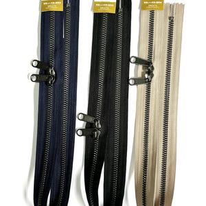 Puede incluir: Tres cremalleras YKK Metaluxe en azul marino, negro y beige. Cada cremallera tiene un tirador de metal y se muestra verticalmente. Las cremalleras son nuevas y tienen etiquetas.