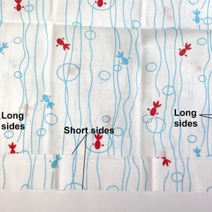 May include: A white fabric featuring a repeating pattern of red and light blue stylized fish shapes, interspersed with light blue vertical wavy lines and circles. The fabric includes black text labels pointing to the long sides and short sides.