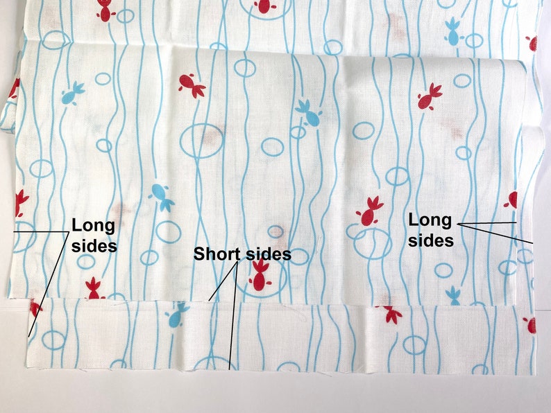 May include: A white fabric featuring a repeating pattern of red and light blue stylized fish shapes, interspersed with light blue vertical wavy lines and circles. The fabric includes black text labels pointing to the long sides and short sides.