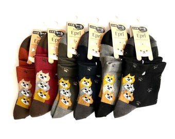 May include: Six pairs of crew socks in various colors including rust, maroon, olive, navy, gray, and black. Each pair features a stacked graphic of three dog faces and small paw prints. The socks are attached to cardboard tags labeled Trois Epri.