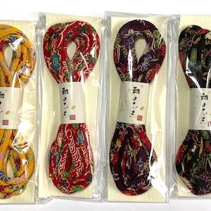 Peut inclure: Quatre bobines de cordon en tissu à motifs colorés, chacune emballée dans du plastique transparent et étiquetée avec des caractères japonais. Les cordons sont en jaune, rouge, violet et noir.