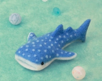 May include: A blue and white felt whale shark with white spots. The whale shark is lying on a light blue surface.