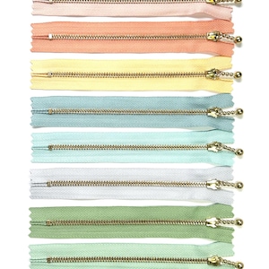 Peut inclure: Assortiment de 12 fermetures éclair de différentes couleurs pastel, dont le rose, la pêche, le jaune, le bleu clair, le vert menthe et le beige. Chaque fermeture éclair est dotée d'un curseur et d'une tirette en métal doré.
