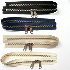 May include: Four zipper closures in different colors: black, navy blue, beige, and white. Each zipper has two pull tabs with silver metal teeth.
