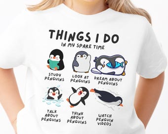 May include: A white short-sleeved t-shirt featuring the text "THINGS I DO IN MY SPARE TIME" above six cartoon penguin illustrations with captions: "STUDY PENGUINS," "LOOK AT PENGUINS," "DREAM ABOUT PENGUINS," "TALK ABOUT PENGUINS," "THINK ABOUT PENGUINS," and "WATCH PENGUIN VIDEOS."