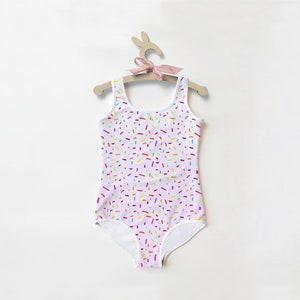 May include: A white one-piece swimsuit with a pink base and a colorful sprinkle pattern.