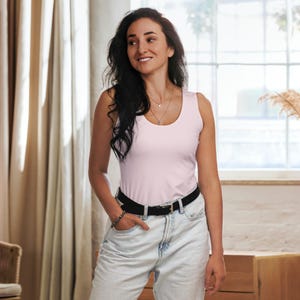 May include: A light pink tank top with a scoop neck and a black belt. The tank top is worn with light-wash denim jeans. The person is wearing a silver necklace and bracelet.