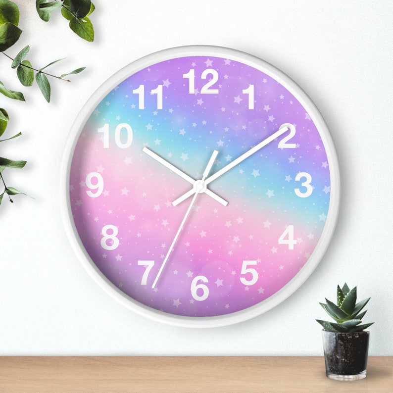 May include: A white clock with a pink, purple, and blue ombre background. The clock face has white numbers and a white star pattern. The clock hands are white.