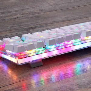 May include: A white mechanical keyboard with rainbow LED lights. The keyboard has a clear plastic case and is illuminated with a variety of colors.