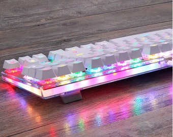 Op de afbeelding: Een wit mechanisch toetsenbord met regenboogkleurige LED-verlichting. Het toetsenbord heeft een transparante kunststof behuizing en wordt verlicht met verschillende kleuren.