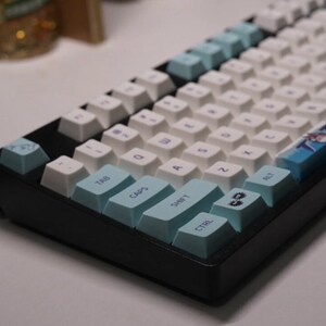 May include: A black mechanical keyboard with white keycaps and blue accent keys. The keyboard has a blue and white design on the right side with the text "TOTO" printed on it.