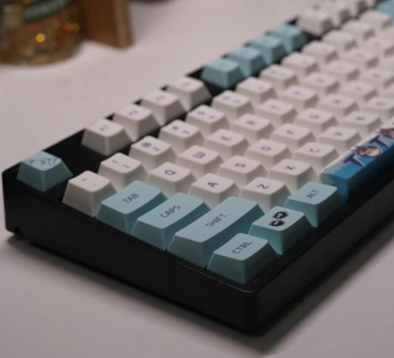 May include: A black mechanical keyboard with white keycaps and blue accent keys. The keyboard has a blue and white design on the right side with the text "TOTO" printed on it.