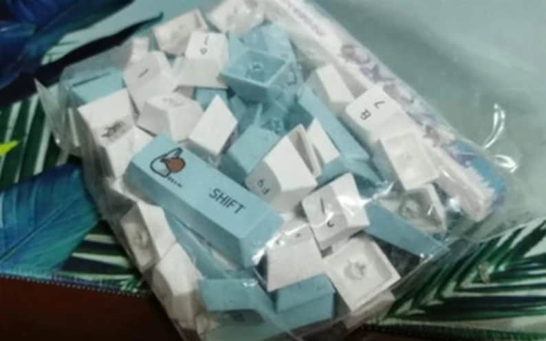 May include: A plastic bag filled with a variety of blue and white keycaps for a mechanical keyboard. The keycaps have different letters and symbols printed on them, including a "SHIFT" keycap.