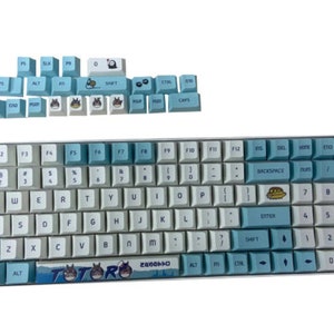 May include: A blue and white keyboard with a Totoro design. The keyboard has a light blue and white color scheme with a Totoro character printed on the space bar. The keyboard has a standard layout with function keys, number keys, and letter keys.