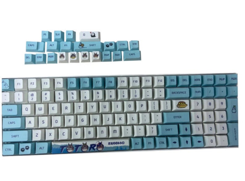 May include: A blue and white keyboard with a Totoro design. The keyboard has a light blue and white color scheme with a Totoro character printed on the space bar. The keyboard has a standard layout with function keys, number keys, and letter keys.