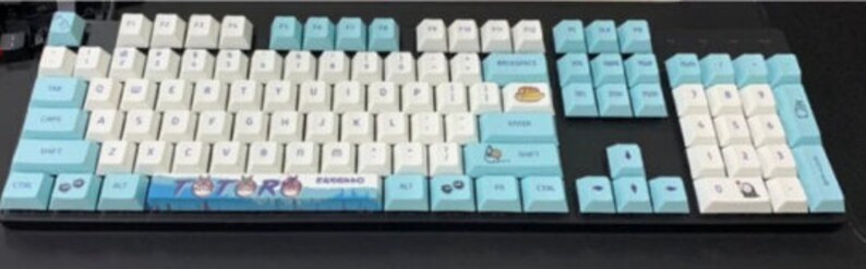 May include: A blue and white keyboard with a Totoro themed keycap set. The keyboard has a black frame and a blue and white keycap set with a Totoro design. The keycaps are made of PBT plastic and have a smooth, matte finish.