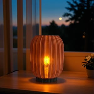 May include: A decorative, ribbed, peach-colored lamp with a warm, glowing light inside. The lamp sits on a dark gray base and is placed on a wooden surface. The background shows a window with a view of a sunset.