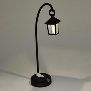 May include: A black table lamp with a curved arm and a small lantern on top. The lantern has a clear glass panel and a white light inside. The base of the lamp is black and has a white foot.