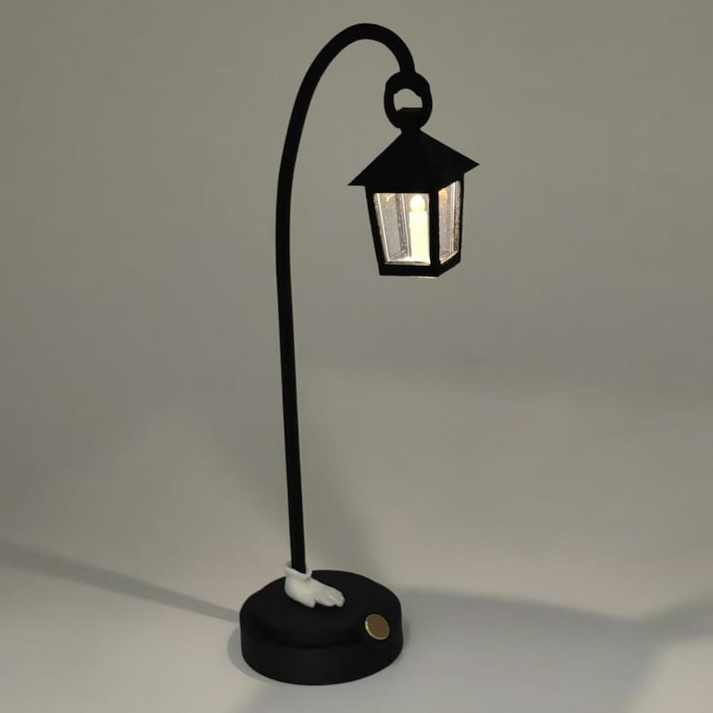 May include: A black table lamp with a curved arm and a small lantern on top. The lantern has a clear glass panel and a white light inside. The base of the lamp is black and has a white foot.