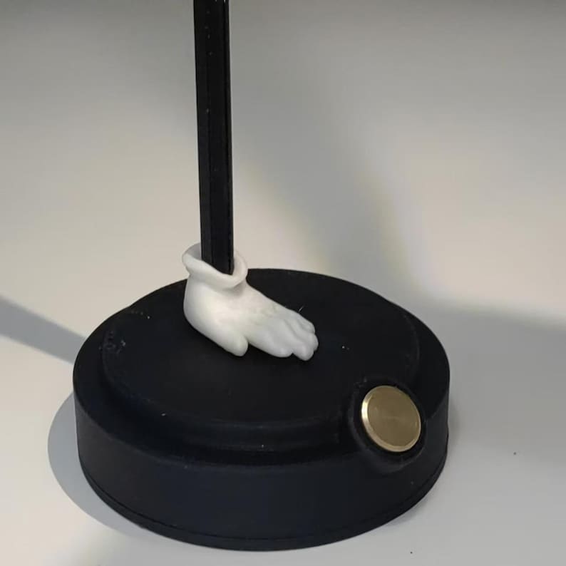 May include: A black and white figurine with a white hand and a black base. The base has a gold metal disc on the side.